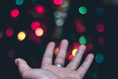 Cropped image of hand on illuminated multi colored lights