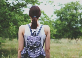 Rear view of backpack woman standing on grassy field