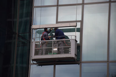 Low angle view of window washers cleaning glass building