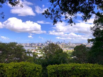Trees and buildings in city against cloudy sky