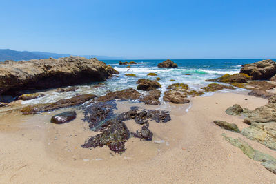 Scenic view of rocks on beach against clear sky