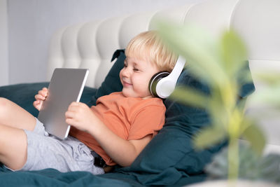 Rear view of boy using mobile phone while sitting on bed