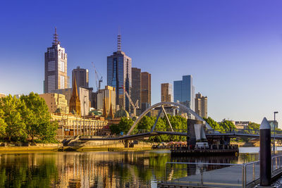 View of city buildings by river against clear sky