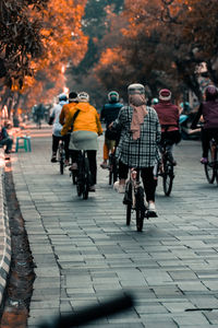 Rear view of people riding bicycle on footpath