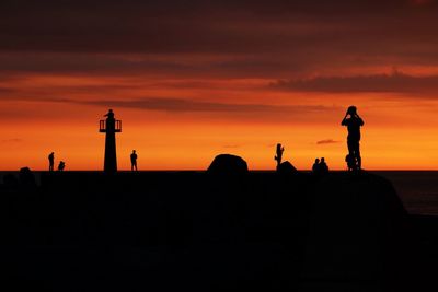 Silhouette people standing by sculpture against orange sky