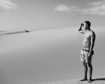 Full length of shirtless man standing at beach against sky