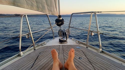 Low section of person on sailboat sailing in sea against sky