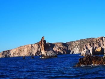 Rock formations in sea against clear blue sky