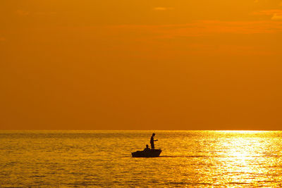 Silhouette boat sailing on sea against orange sky