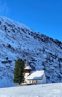Scenic view of little church and snowy swiss mountains against clear blue sky