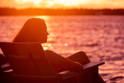 Low angle view of woman sitting by sea against sky during sunset