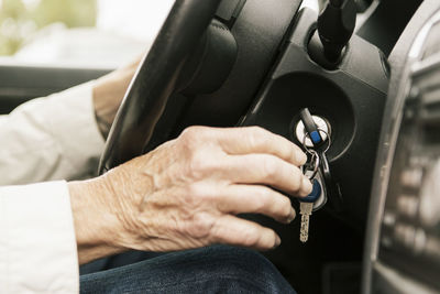 Cropped image of senior woman putting car key in ignition lock