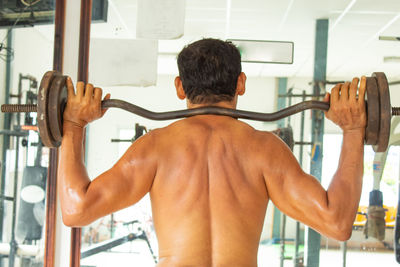 Rear view of shirtless man exercising at gym