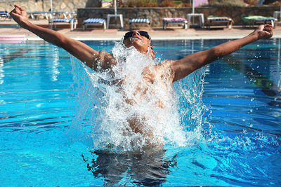 Man with arms outstretched splashing water in swimming pool