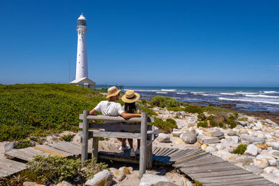 Lighthouse by sea against clear blue sky