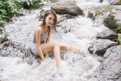 Full length of young woman splashing water in rocks