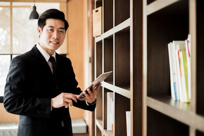 Portrait of businessman using digital tablet by bookshelf