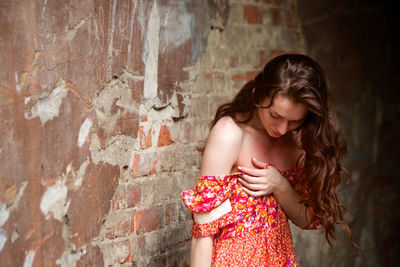 Young woman in dress standing against wall