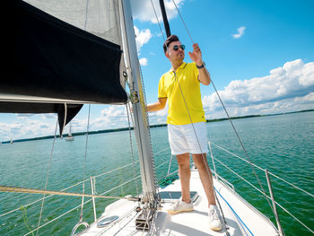 Handsome young person standing on a sailboat bow and looking at side in sunny summer day person