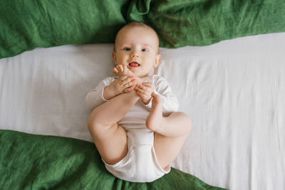 Top view of a charming smiling caucasian 6-month-old boy dressed in a bodysuit, holding his legs