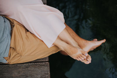 Low section of couple relaxing on pier over lake