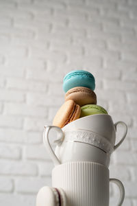 Stack of white coffee cups filled with macaroons on the edge of the table, white brick wall backgro