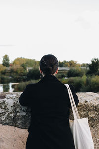 Side view of young woman standing against sky