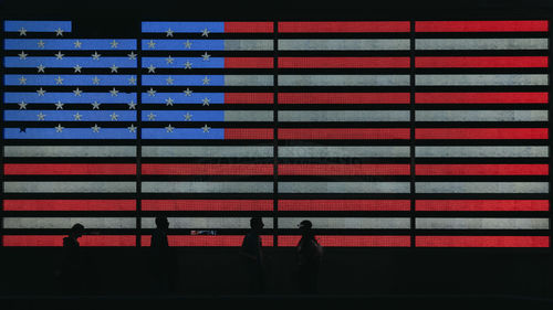 Silhouette people standing by illuminated american flag at night