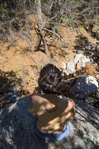 High angle view of topless woman sitting on rock in forest