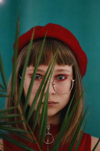 Close-up portrait of teenage girl wearing eyeglasses with plant standing against wall