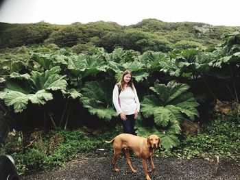 Portrait of young woman with dog standing on field against trees