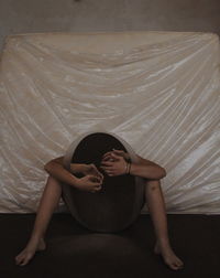 Low section of naked woman holding mirror while sitting against bed in room