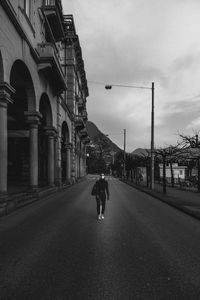 Rear view of girl walking on empty street amidst buildings in isolated city during covid-19.