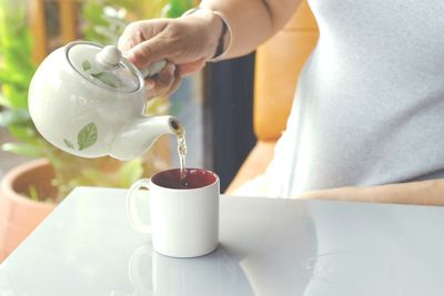 Midsection of woman pouring coffee cup on table