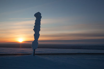 Snow covered pole on field against sky during sunset