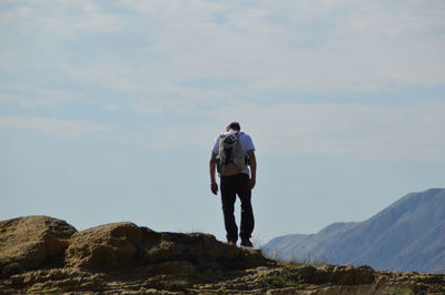 Rear view of hiker standing on rock formation at mountain against sky