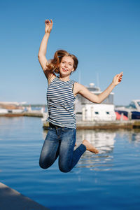 Portrait of smiling young woman jumping at harbor