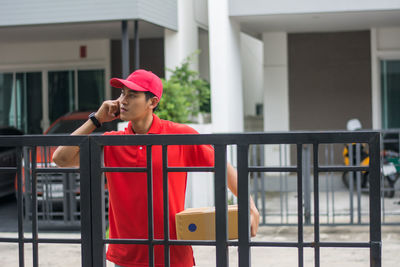 Delivery man standing at closed gate against buildings