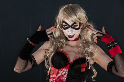 Portrait of woman in harley quinn cosplay costume making handgun sign against wall