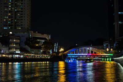 Illuminated city by river against sky at night