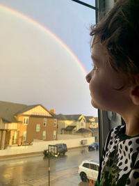 Side view of boy looking at a rainbow through a window