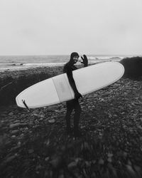 Side view of man with surfboard standing on beach