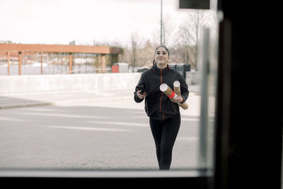 Smiling young delivery woman holding packages while walking on road