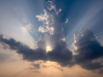 Low angle view of sunlight streaming through clouds