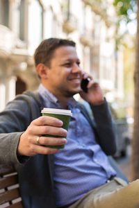 Young man walking on the street, drinking coffee to go and talking by his phone.. outdoors, urban