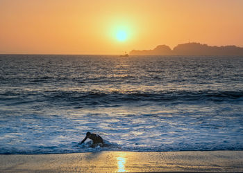 Scenic view of sea against sky at sunset. swimmer crawls out, fishing boat offshore. man overboard.