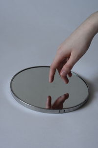 Cropped hand of person reaching towards mirror over white background
