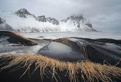 Scenic view of sea by snowcapped mountains against sky