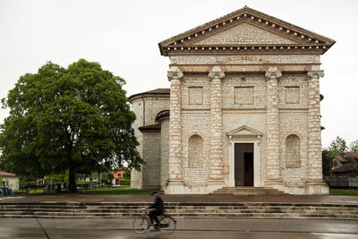 Man riding bicycle on street by building against sky