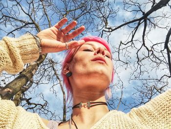 Low angle portrait of woman with bare tree against sky